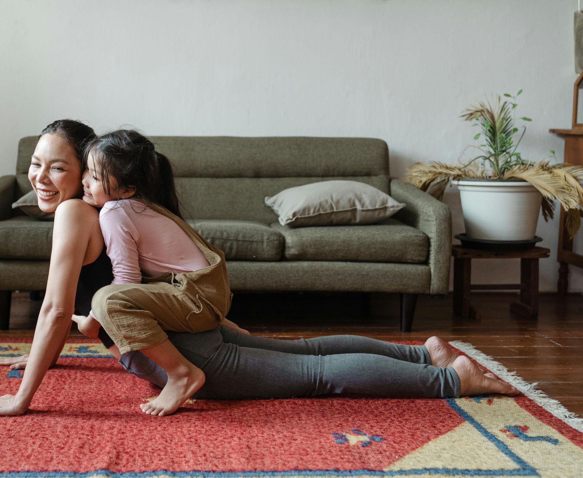 A joyful mother practicing yoga with her daughter on a colorful rug indoors.