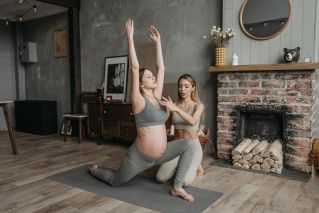 Pregnant woman doing yoga poses with a trainer in cozy indoor setting.